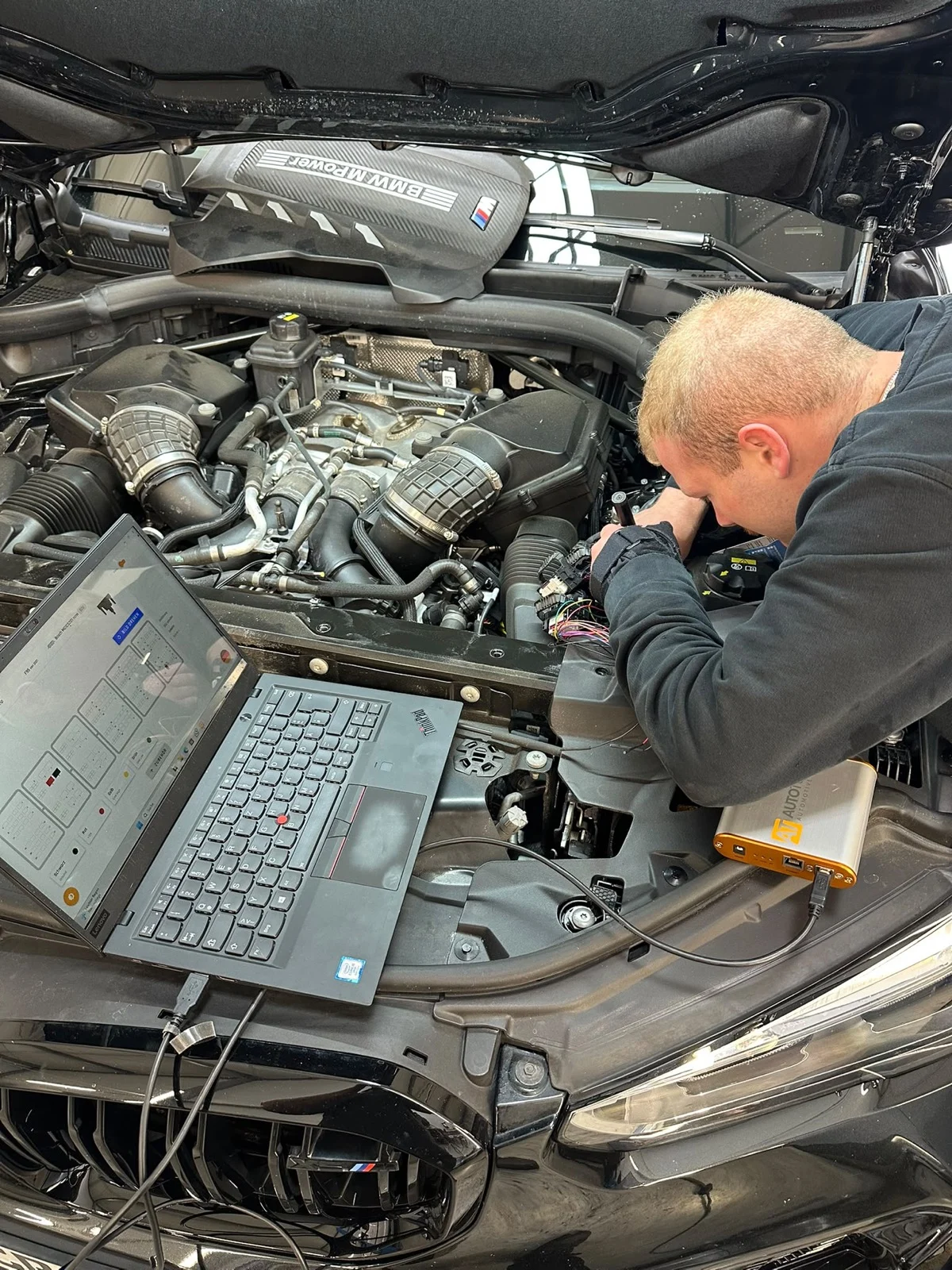 Techniker arbeitet mit Laptop und Programmier-Interface am geöffneten Motorraum